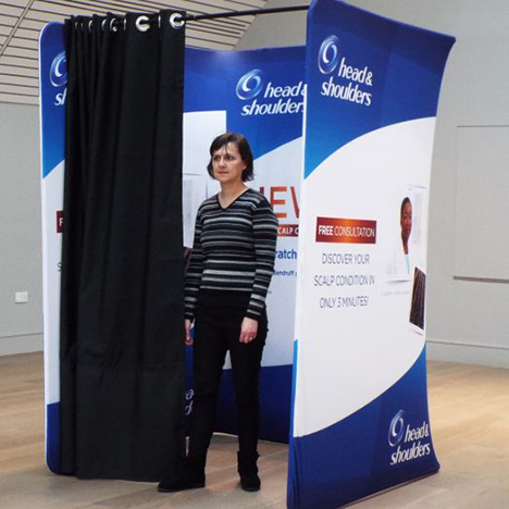 Branded pop-up changing booth advertising Head and Shoulders products with a woman standing inside the booth